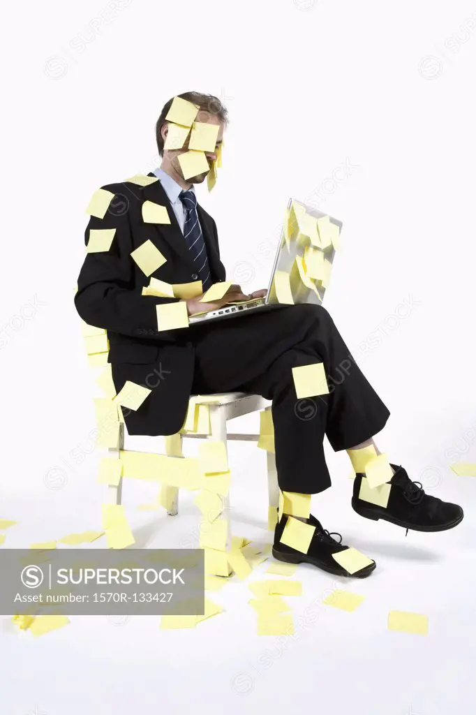 A man covered in blank adhesive notes while sitting and using a laptop