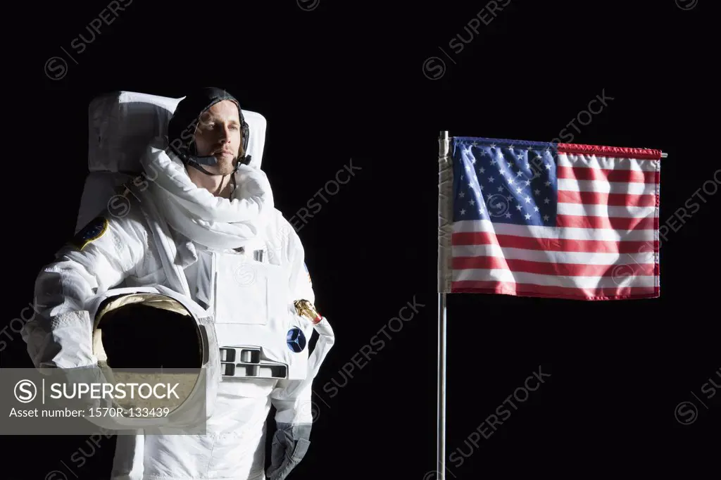 An astronaut holding his helmet standing next to an American flag, portrait