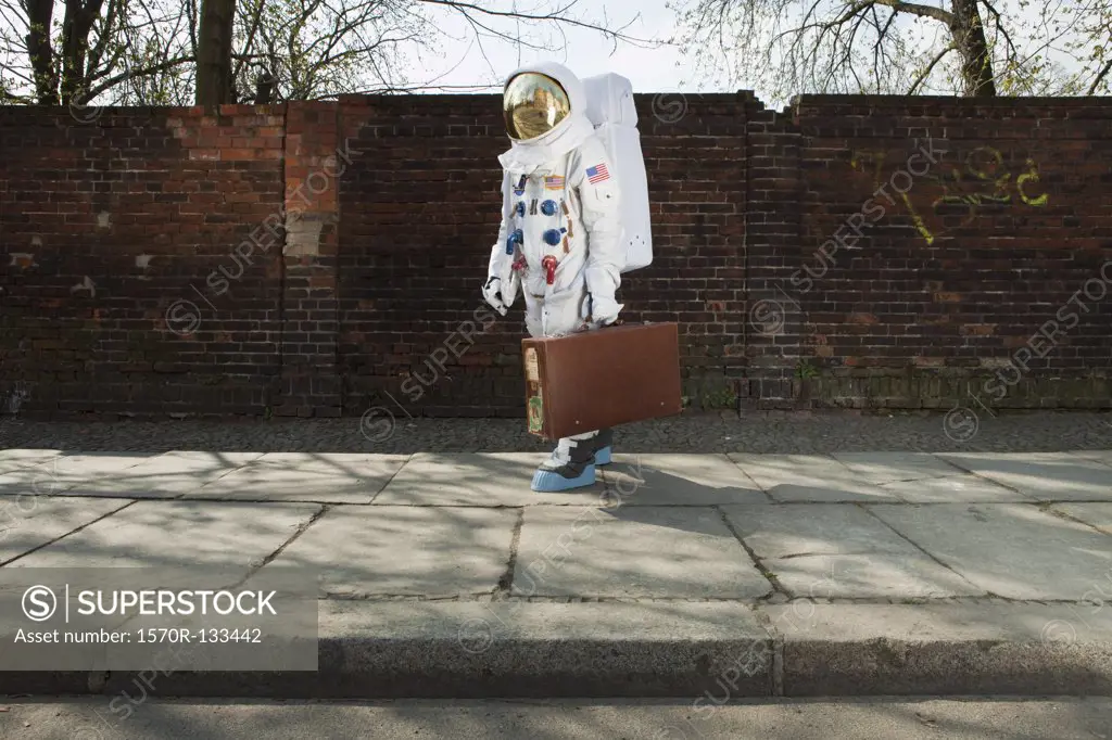 An astronaut carrying a suitcase and walking on a city sidewalk