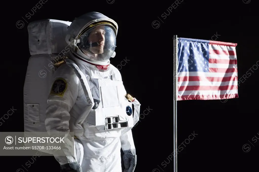 An astronaut with a serious expression standing next to an American flag