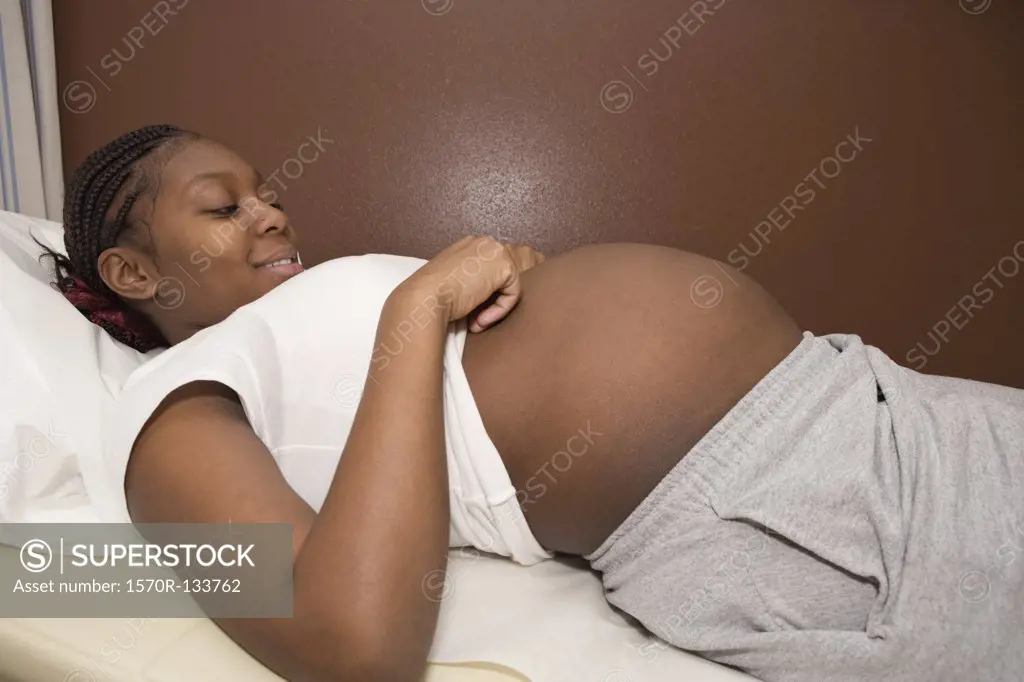 A pregnant woman lying on an exam table smiling down at her abdomen