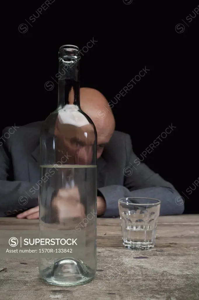 A drunk and depressed businessman with a bottle of vodka and an empty glass