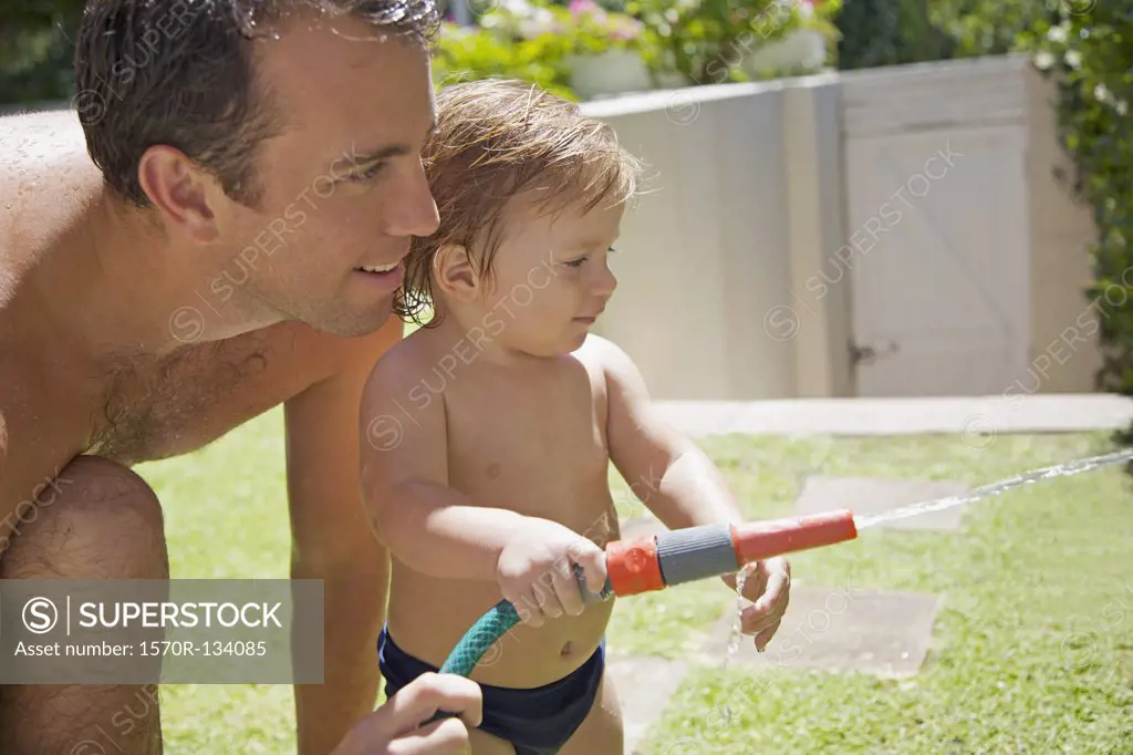 Detail of a man and a baby boy with a garden hose