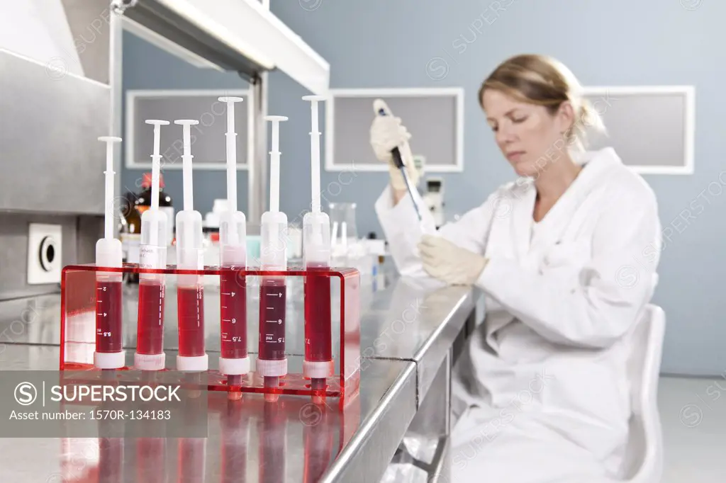 A row of vials holding blood and a lab technician working in background, focus on foreground