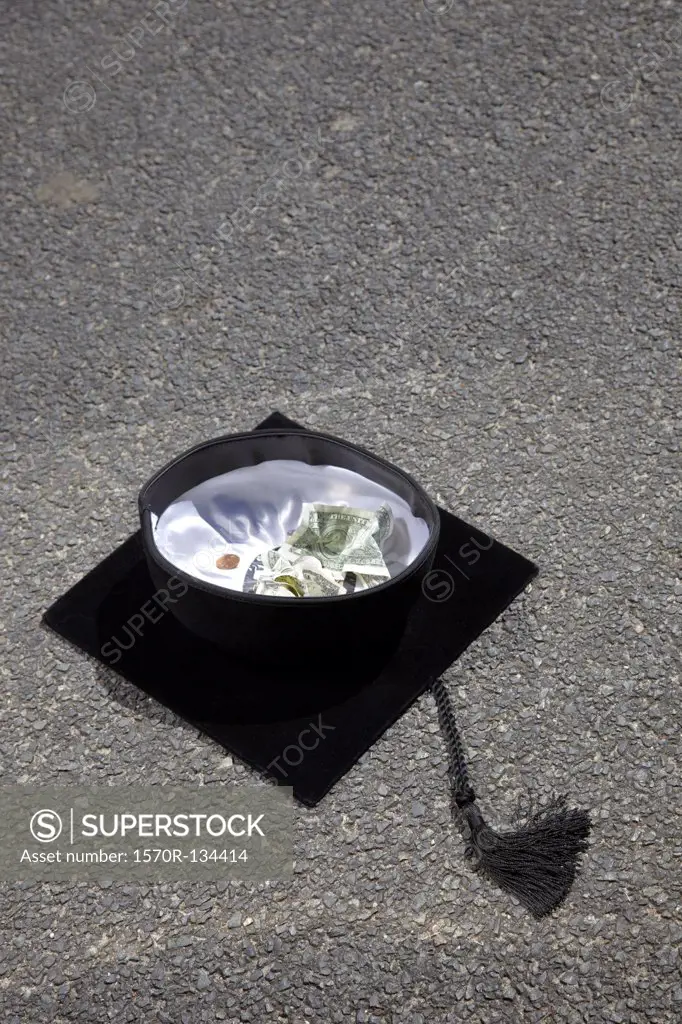Mortarboard with money in it on asphalt