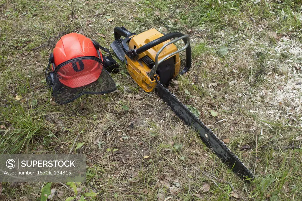 A chainsaw and safety helmet lying on the grass