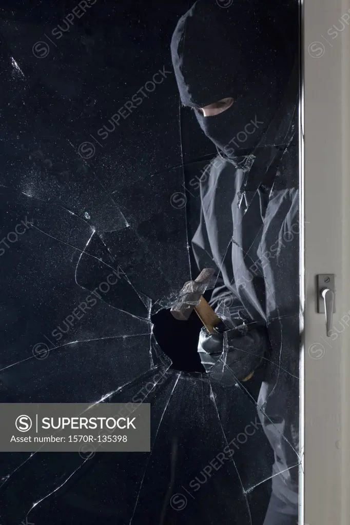 A criminal breaking into a window with a hammer