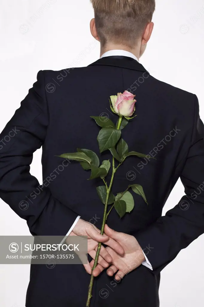 A man holding a rose behind his back, rear view, waist up