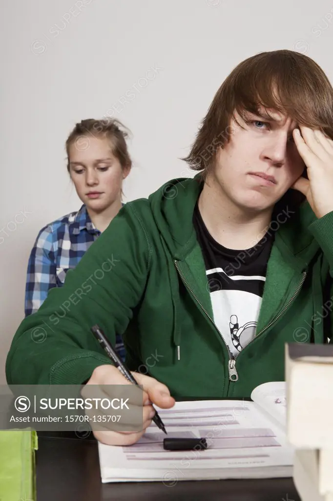 A teenage boy looking worried in a classroom, girl in background