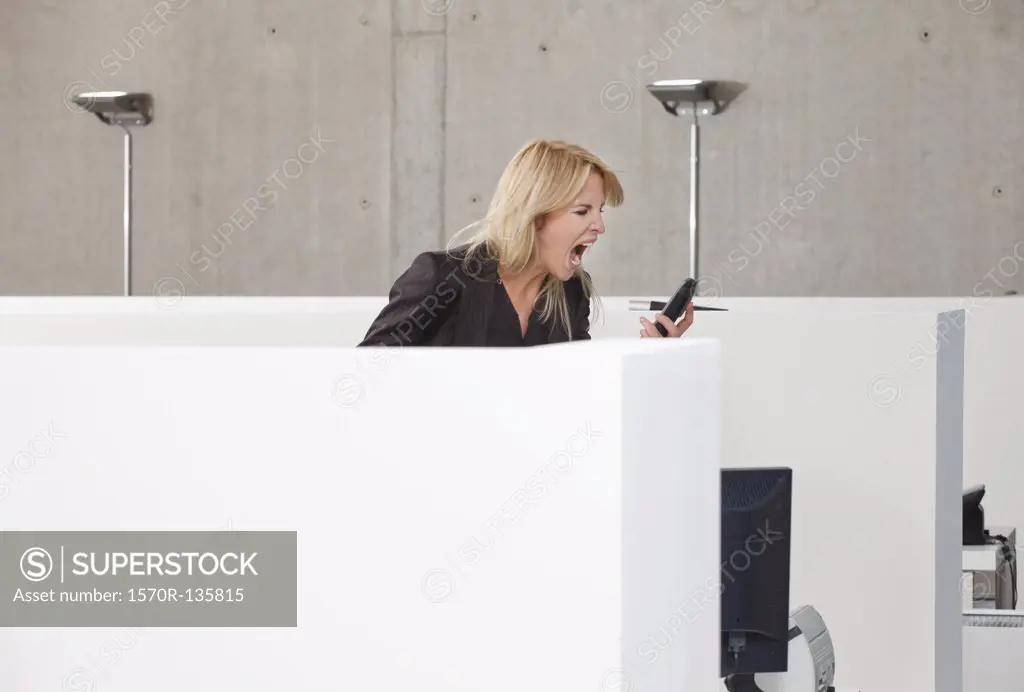 A woman screaming into a mobile phone in an office cubicle