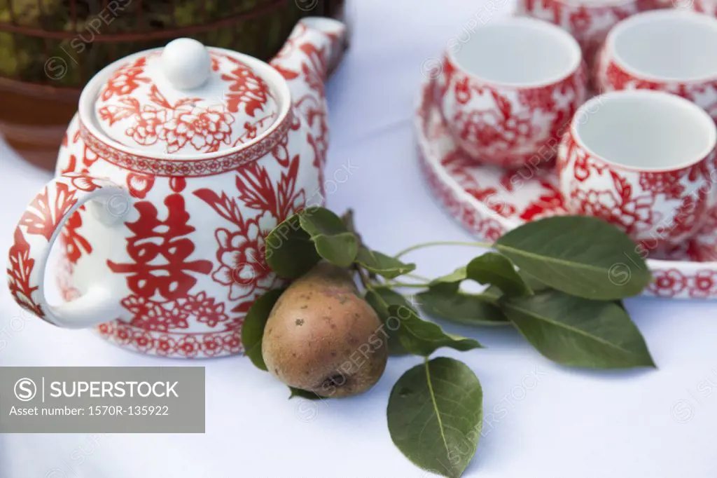 A ceramic tea set and a pear on a table