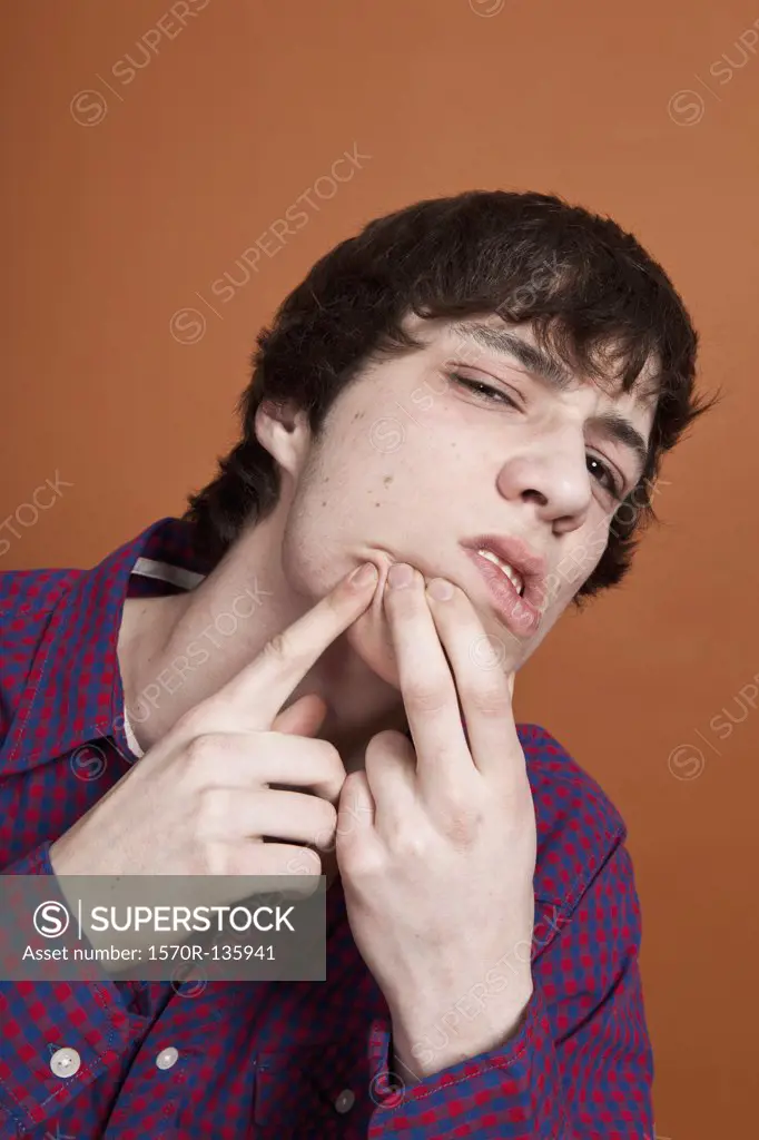 A teenage boy popping a zit on his face, portrait, studio shot