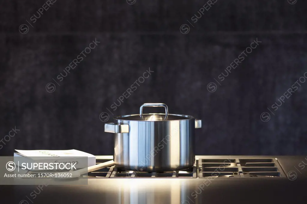 Saucepan, cookery book and wooden spoon on hob.