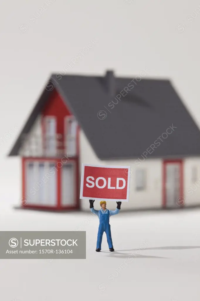 A miniature construction worker figurine holding aloft a SOLD sign