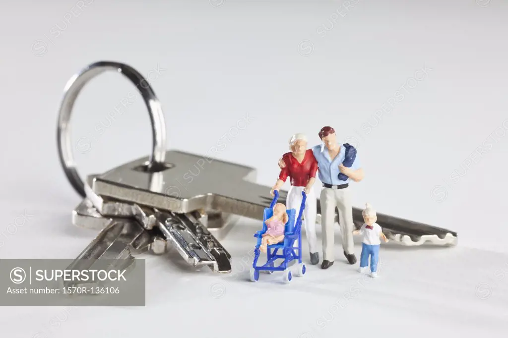 A young family of miniature figurines standing next to house keys on a key ring