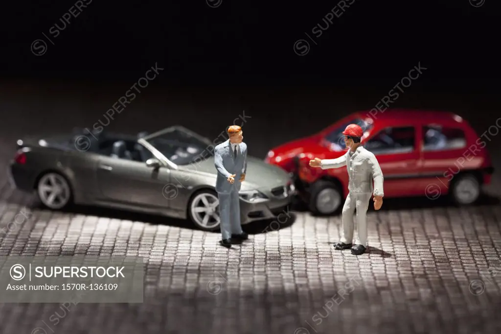 Two miniature figurine men arguing over their miniature crashed cars