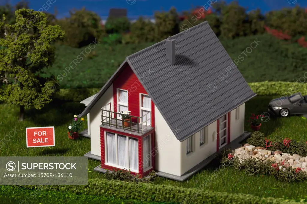 A diorama of a miniature house with a FOR SALE sign