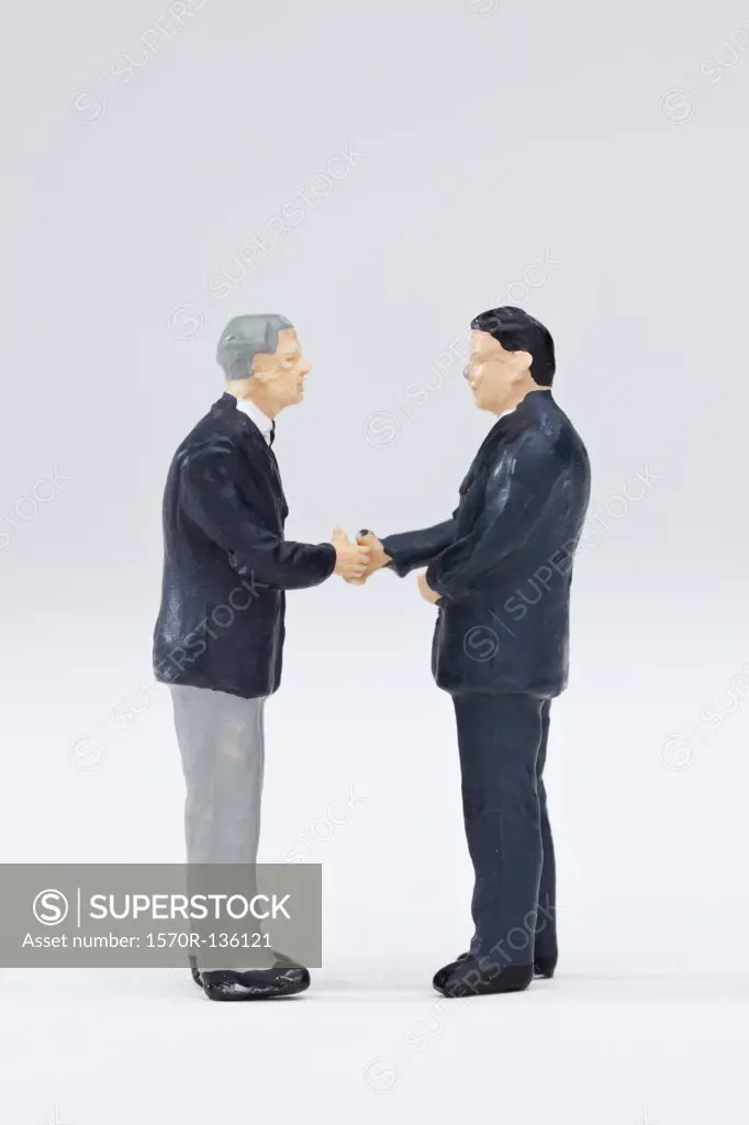 Two miniature businessmen figurines shaking hands