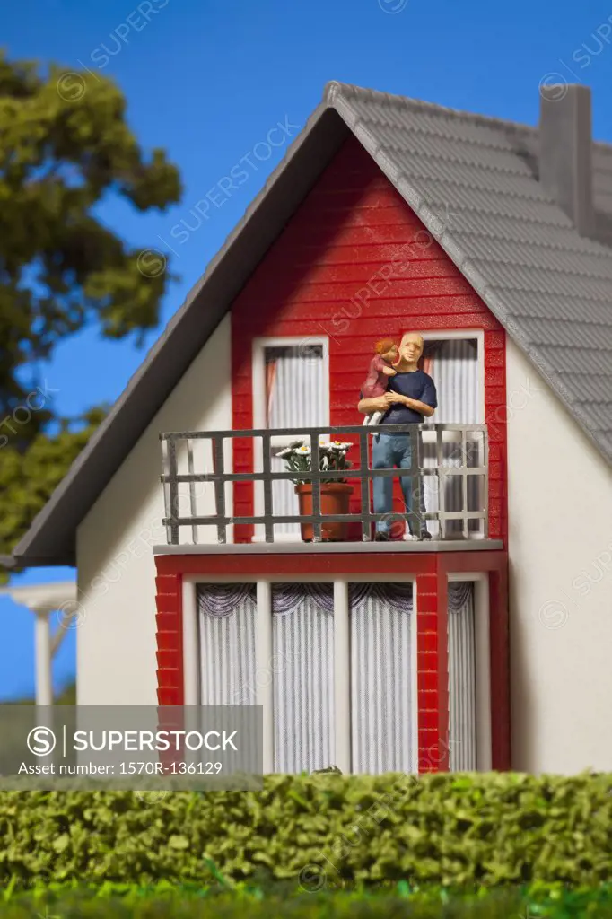 A miniature father figurine holding his daughter on the balcony of a dollhouse