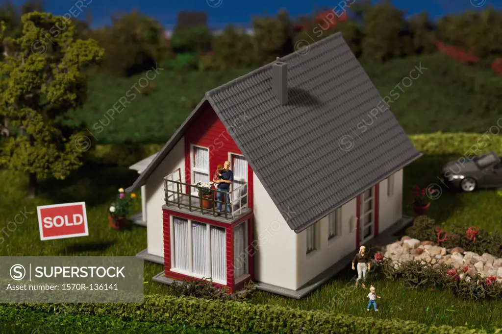 A diorama of a miniature house with a family of figurines and a SOLD sign