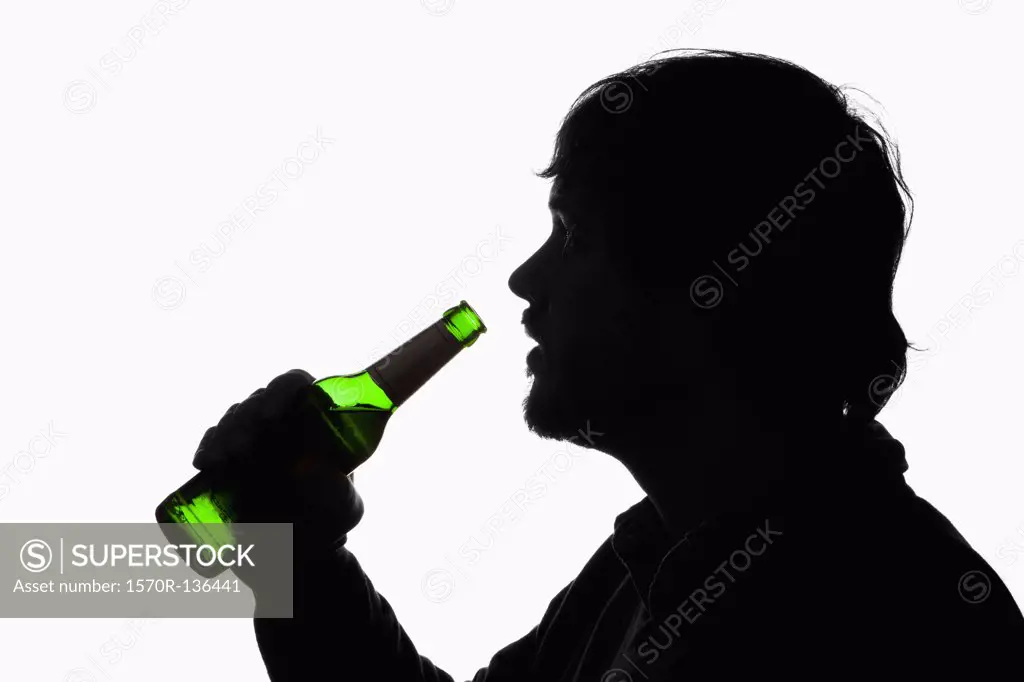 A silhouetted man about to drink from a beer bottle