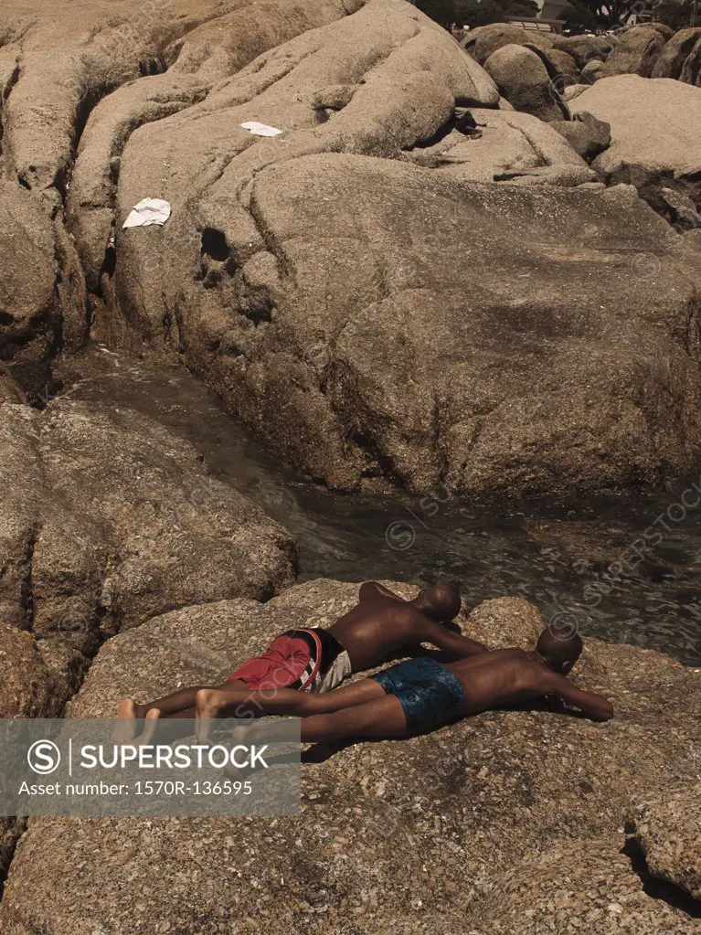 Two men sunbathing on a large rock by a stream