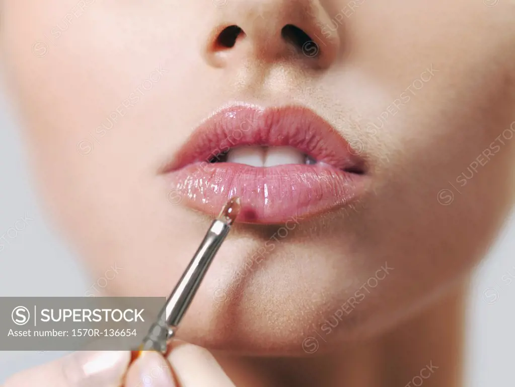 A woman applying lip gloss with a make-up brush, close-up of lips