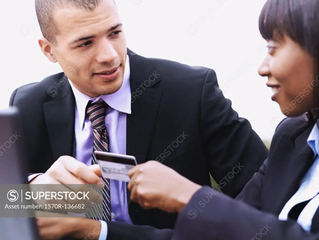 A businesswoman giving a businessman a credit card