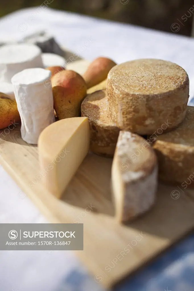 Pears and a variety of cheese on a chopping board on a table outside