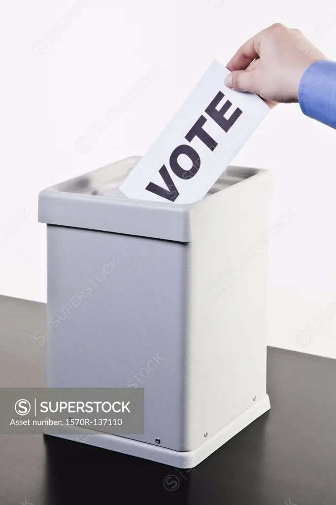 A man putting a ballot with the word VOTE written on it into a ballot box, close-up hands