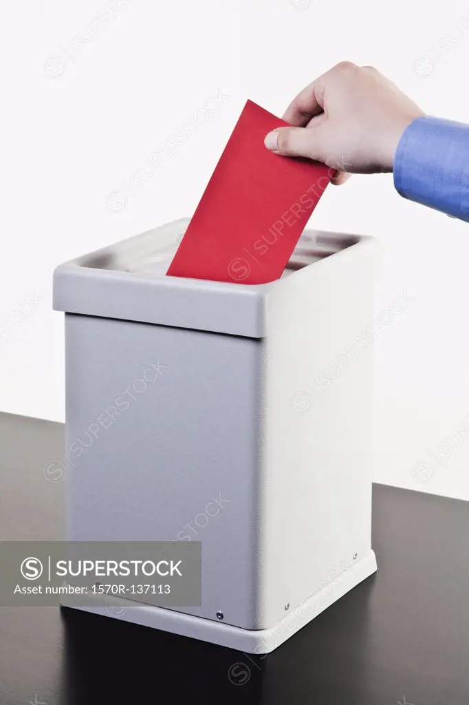 A man putting a blank red ballot into a ballot box, close-up hands