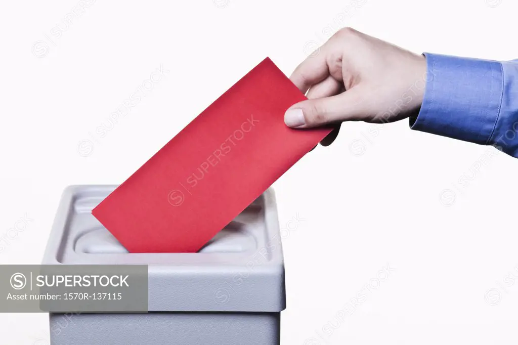 A man putting a blank red ballot into a ballot box, close-up hands