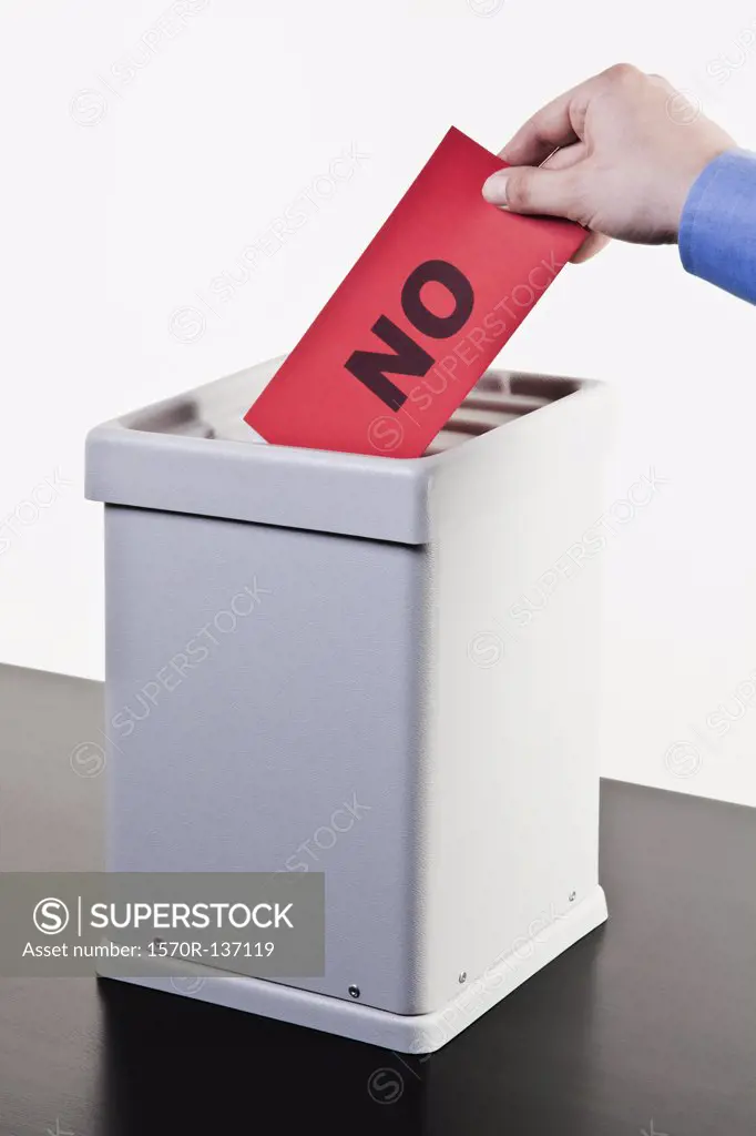 A man putting a ballot with the word NO written on it into a ballot box, close-up hands