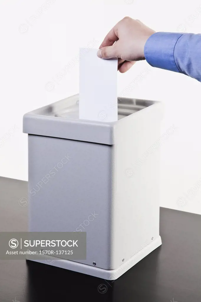 A man putting a blank white ballot into a ballot box, close-up hands