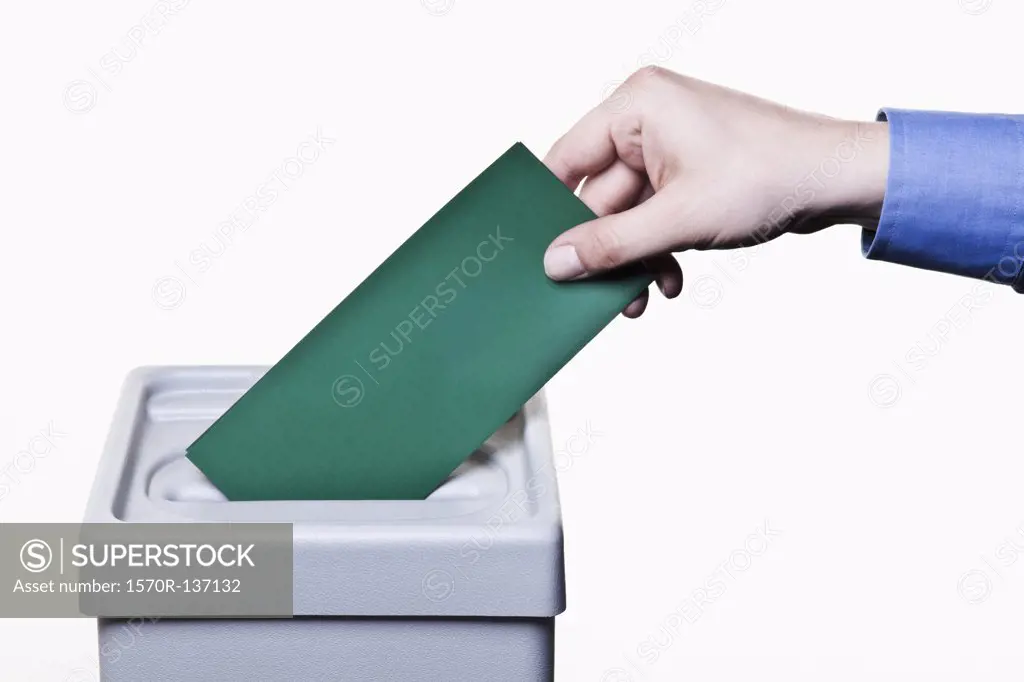 A man putting a blank green ballot into a ballot box, close-up hands