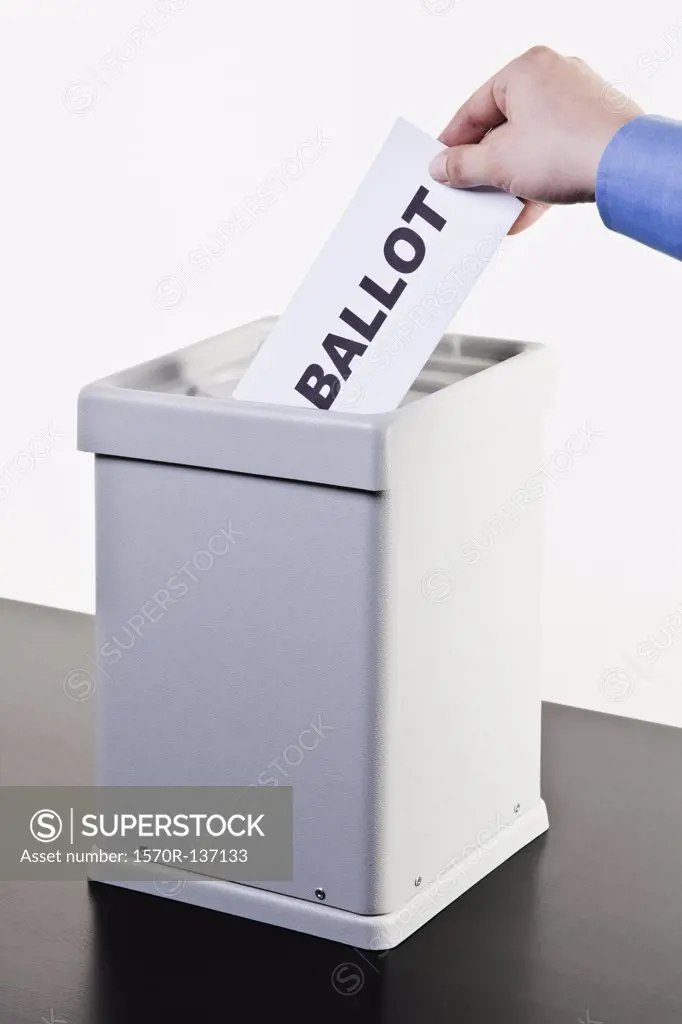A man putting a paper with the word BALLOT written on it into a ballot box, close-up hands