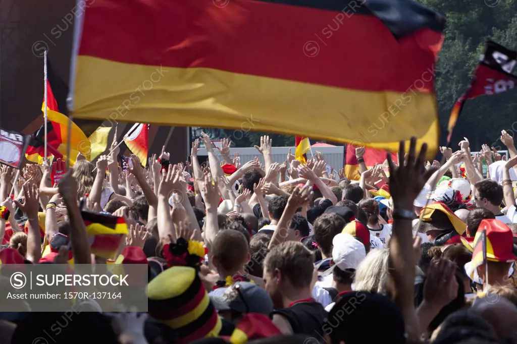 Detail of people in a crowd cheering and waving German flags