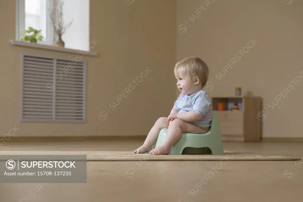 A happy toddler sitting on a potty chair, looking away