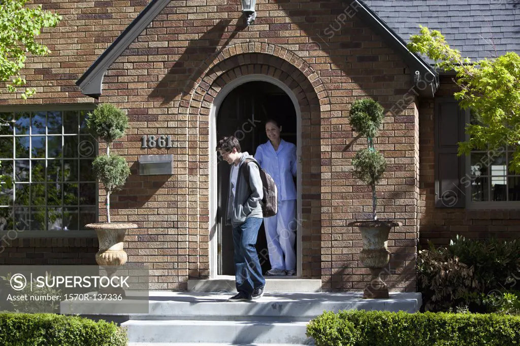 Smiling Mother stands at front door of house as son departs