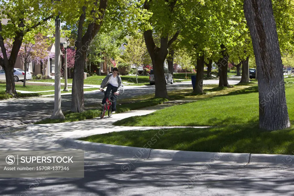Boy riding bike on footpath among roadside trees