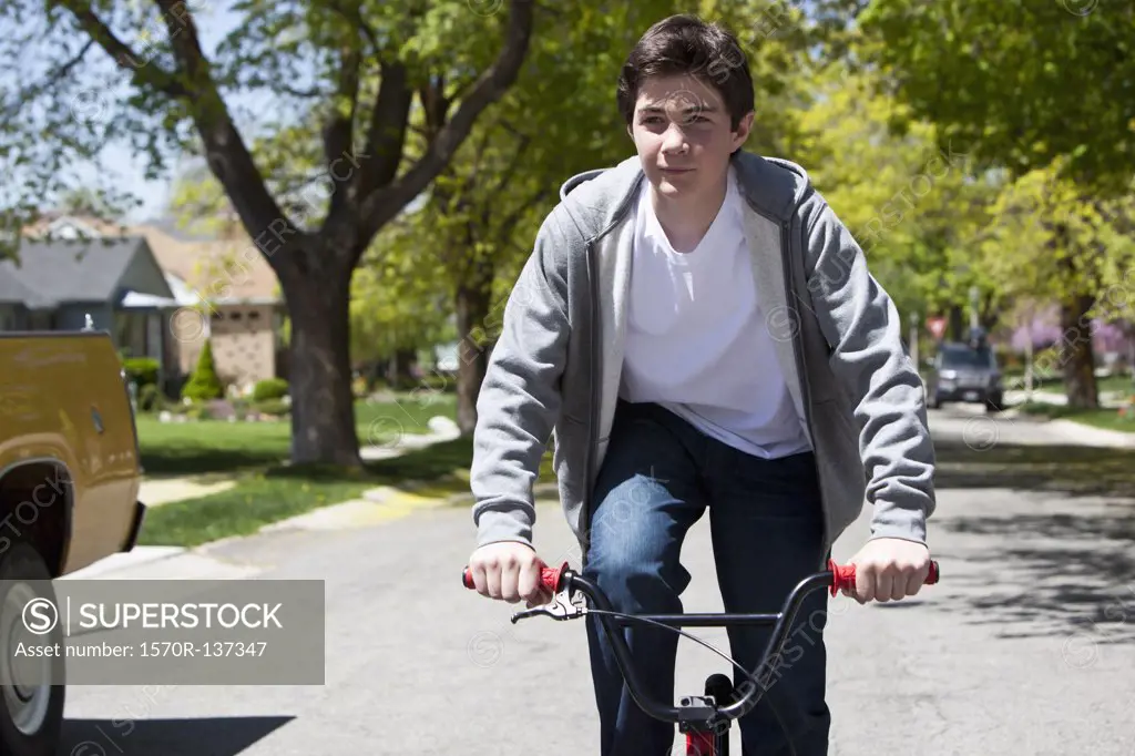 Boy stands while riding bike with a content facial expression