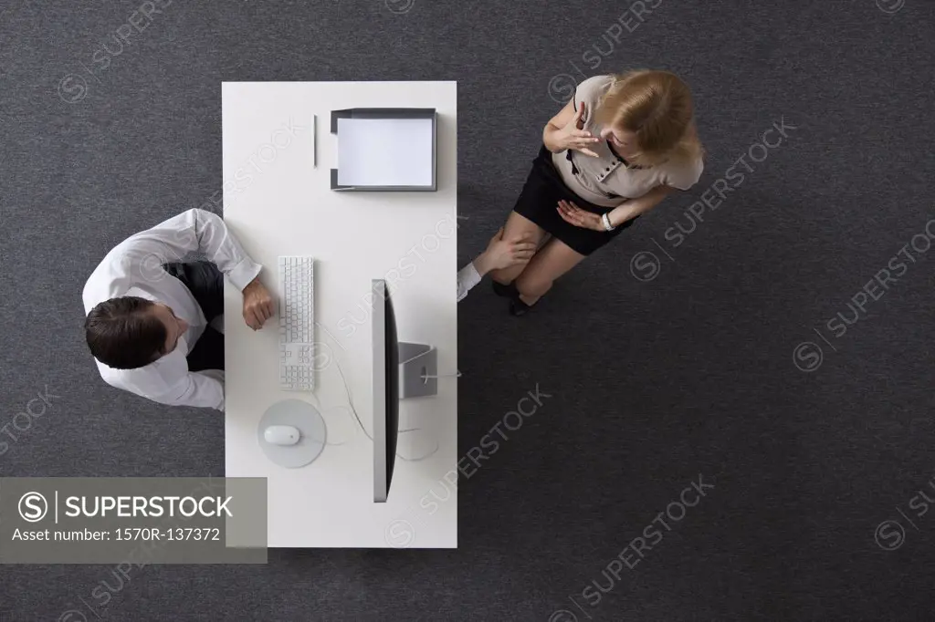 A businessman reaching under a desk to touch a woman's knee, overhead view