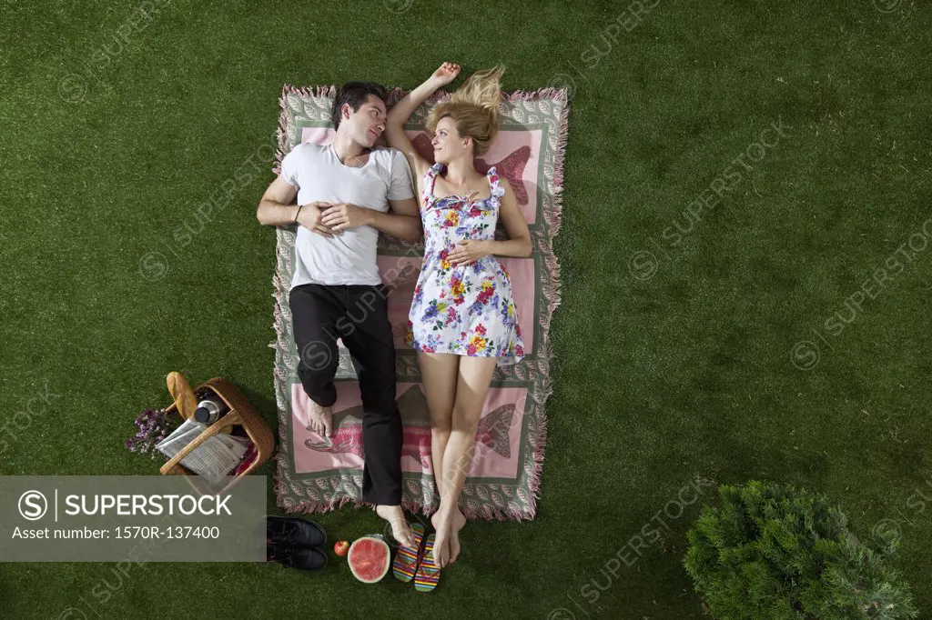 A couple lying on a blanket in a park looking at each other romantically, overhead view