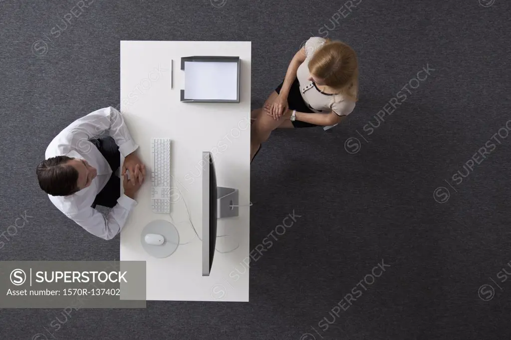 A businessman and businesswoman sitting across a desk from each other, overhead view