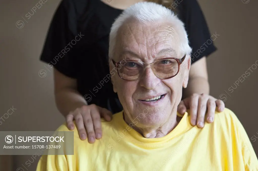 A senior man in a nursing home, hands on his shoulders, focus on him