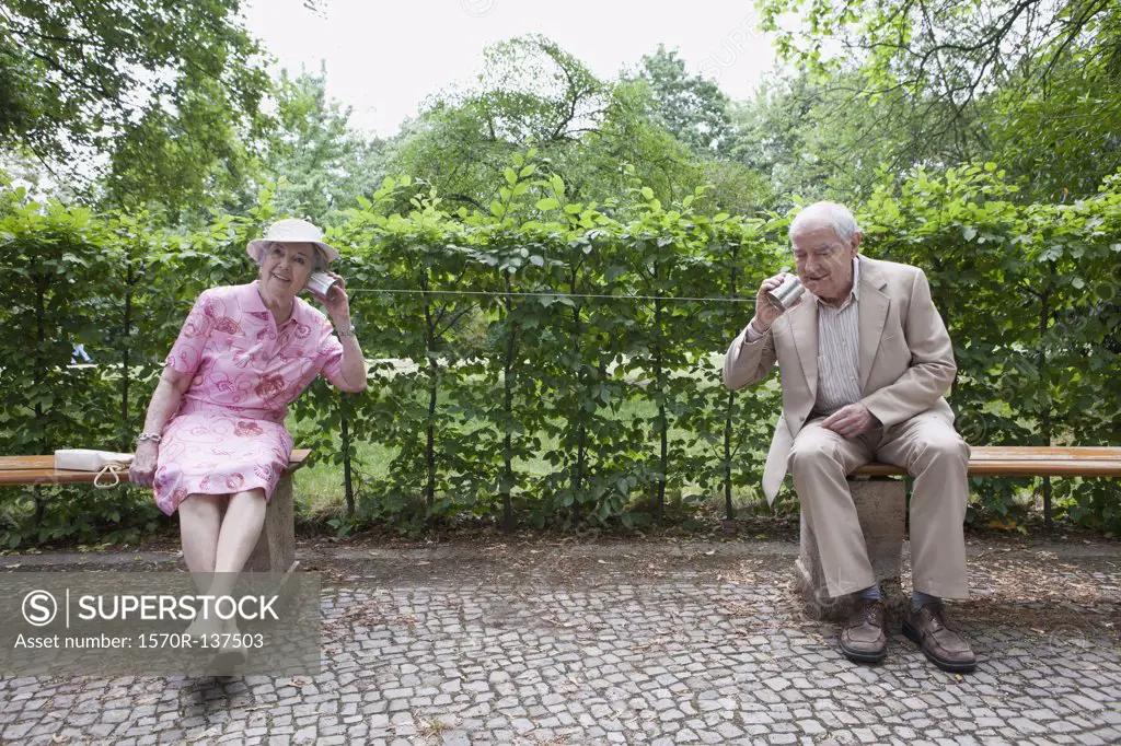 Senior man and woman speak to each other on tin can phones in park