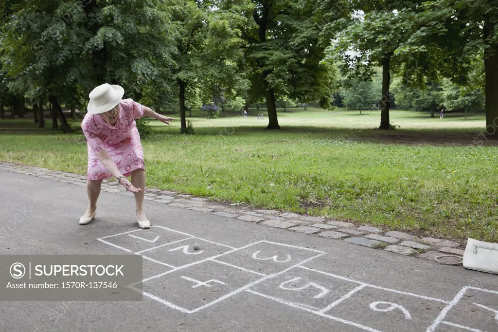 Senior woman rolls a stone as she plays hopscotch