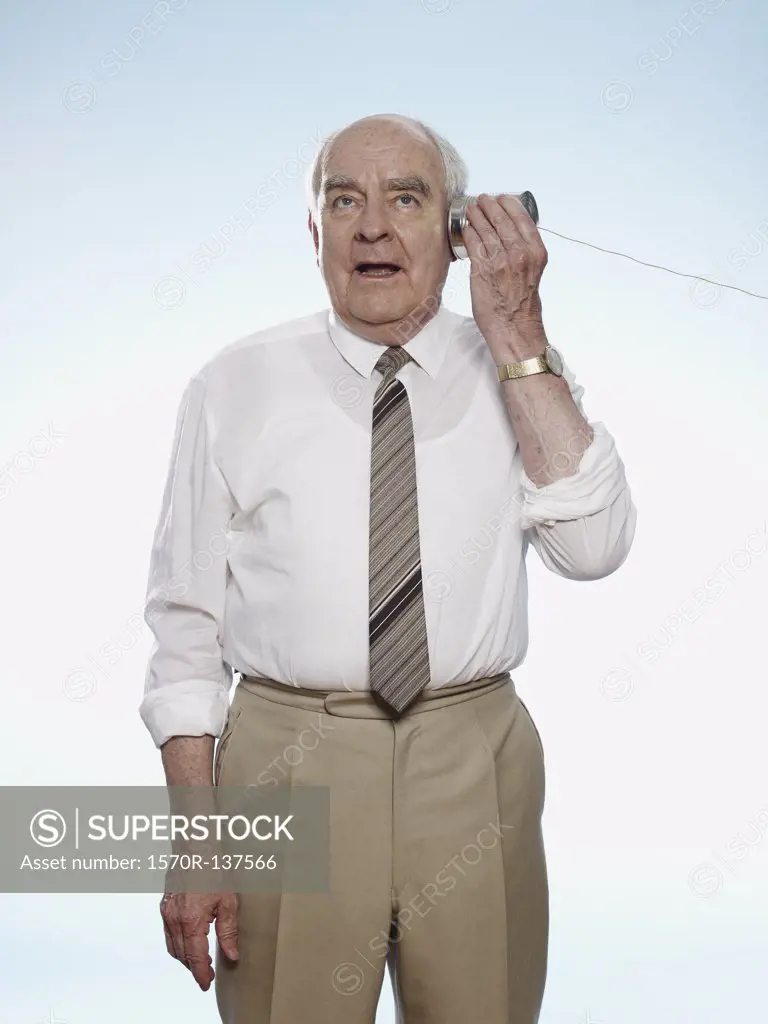 Senior man comically strains to hear on a tin can phone