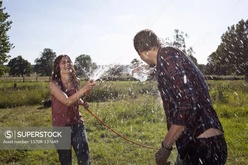 Girl sprays guy with hose on field