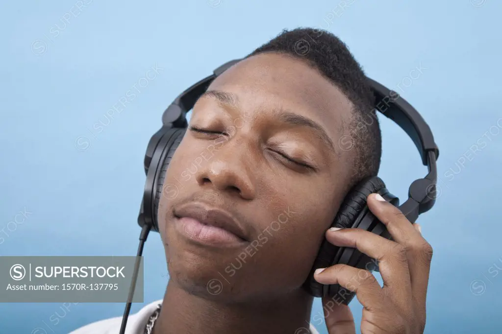 A young man listening to music with headphones, eyes closed